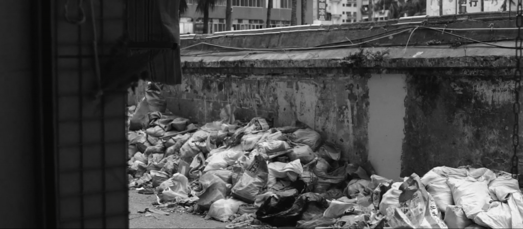 Black and white image of side street with bags of rubble lined up along the side