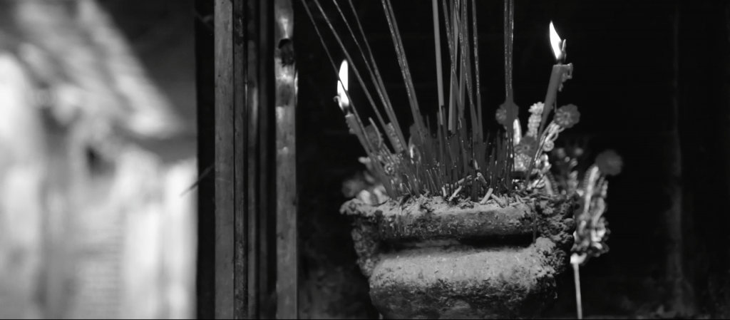 Black and white image of a incense holder in an Chinese shrine, filled with candles, incense and ash