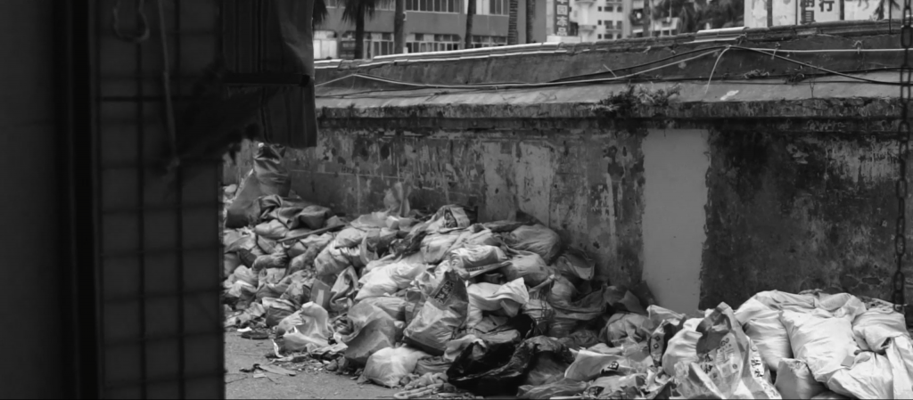 Black and white image of an alleyway with detritus on either side, fallen awnings and rubble