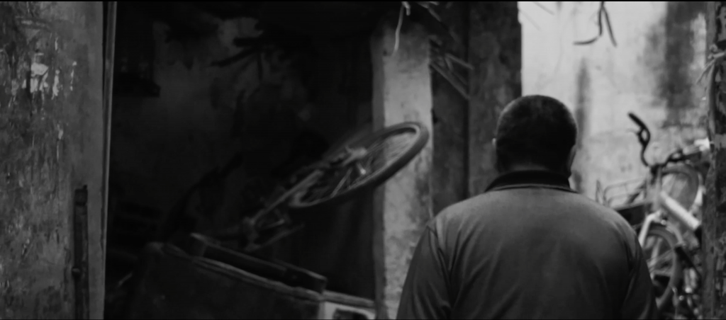 Black and white image of a man with his back to the camera. Pre-pay bikes are piled high in front of him 