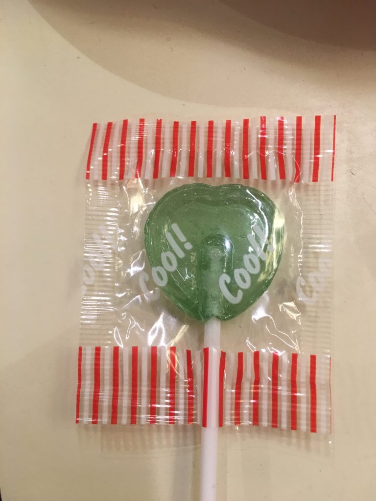 A green heart-shaped lollipop wit the words 'cool!, cool!' written on the wrapper.
