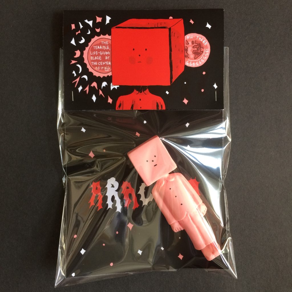 Colour photo of a pink resin figure in clear plastic bag with a black, red and pink title card insert and illustrated cardboard label depicted the square headed figure.