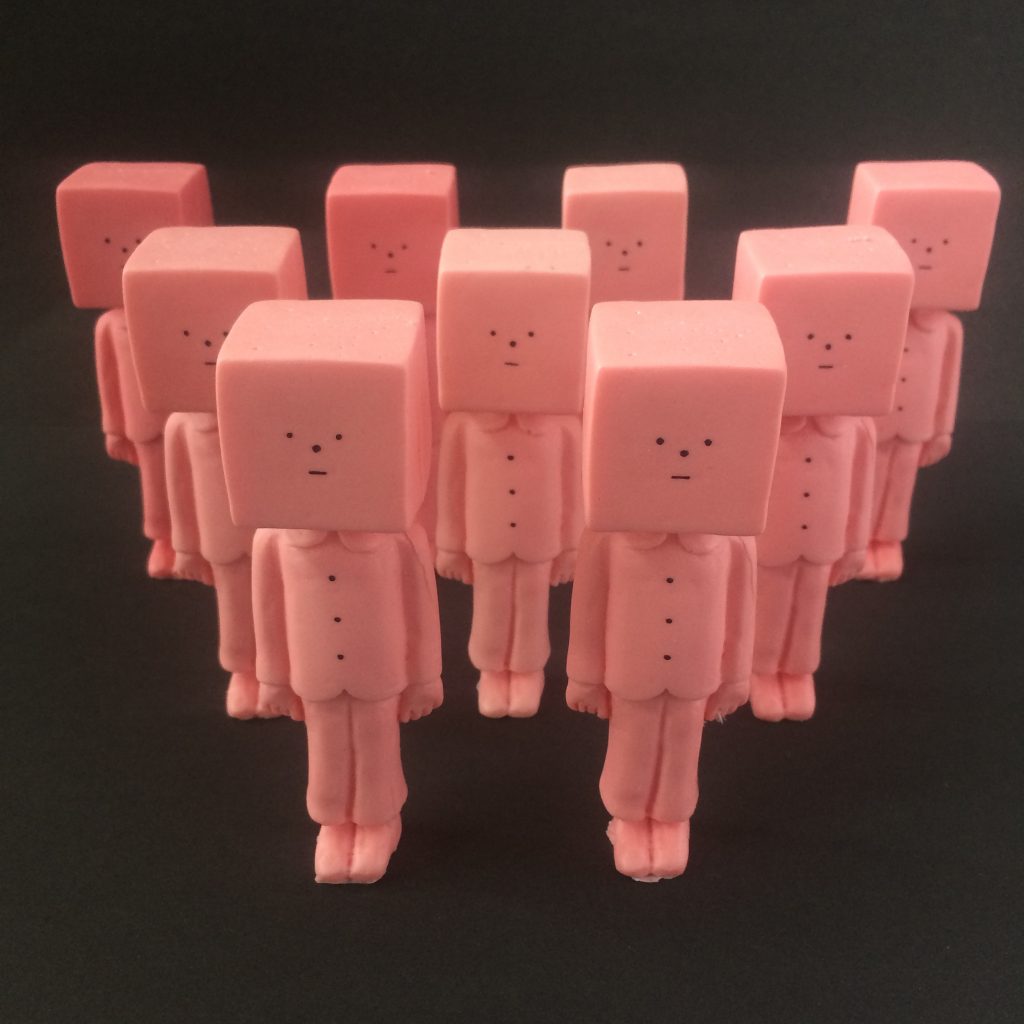 Colour photograph of 9 pink resin figures arranged in a triangle, 4 at the back, 3 in the middle and 2 at the front. 