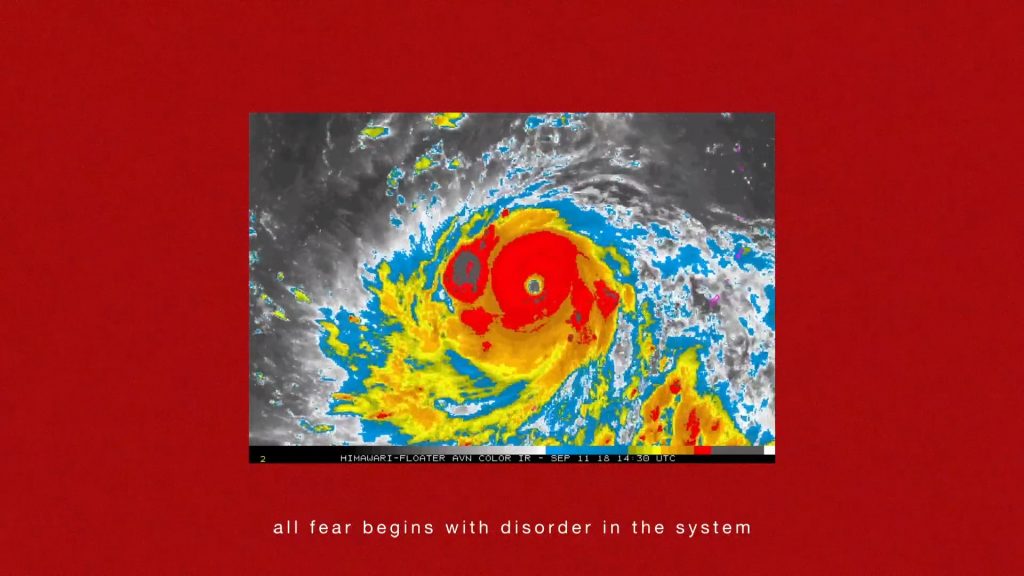 A thermal aerial image of a hurricane swirling in bright red, yellow, blue and black & white is shown in a rectangle, framed by a blood red background. On the bottom of the image white text reads: ‘all fear begins with disorder in the system’.