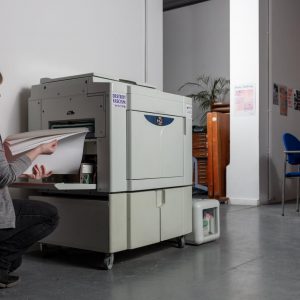 Damien Robinson, a white woman in a pink t-shirt, loading paper in a risograph machine.