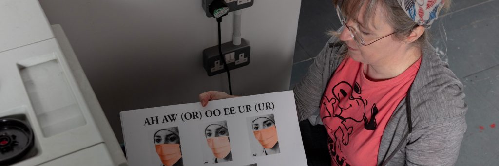 Image of Damien Robinson, a white woman in a pink t-shirt, holding a black and orange Risograph print. 