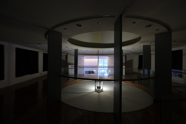 A Installation shot of Hypothesis Atlas and Voyager at the second floor. It's dark circular space with rotating light in the middle. 