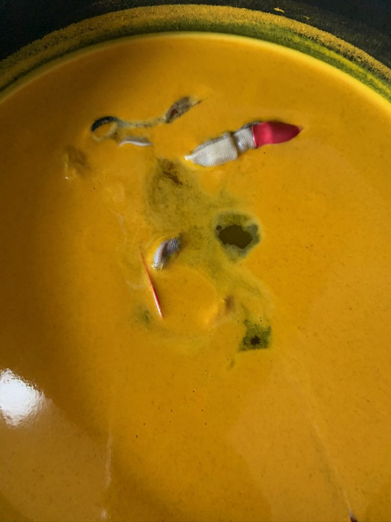 a white finger with a melting red acrylic nail sits in a yellow put of water 