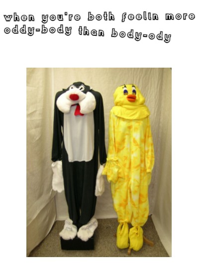 Two costumes hung on stands, one is of Sylvester the cat and the other is Tweety Bird. Sylvester is a black cat with white feet, hands, stomach and cheeks. Tweety is yellow all over with an orange beak and big black eyelashes. They are hung in a small fabric cubicle, the fabric is cream coloured. They look creepy and awkward with no human bodies inside them to fill them out. At the top of the image is some white text with a black background which says 'when you both feel more oddy-body than body-ody'