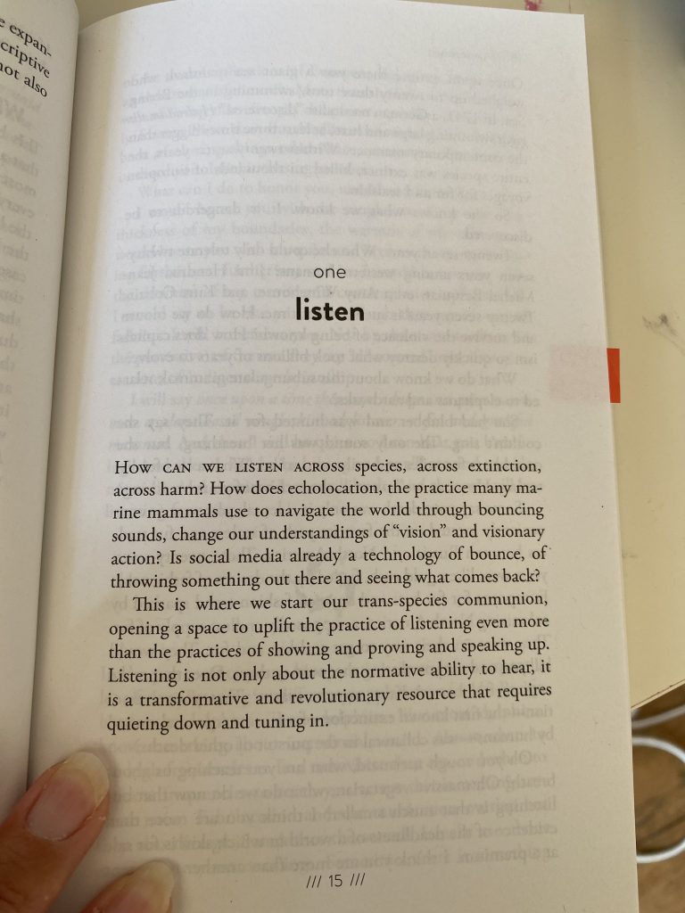 Hand of artist Rebekah Ubuntu holds open Alexis Pauline Gumbs’ book ‘Undrowned: Black Feminist Lessons from Marine Mammals’ on a page titled 'Listen'