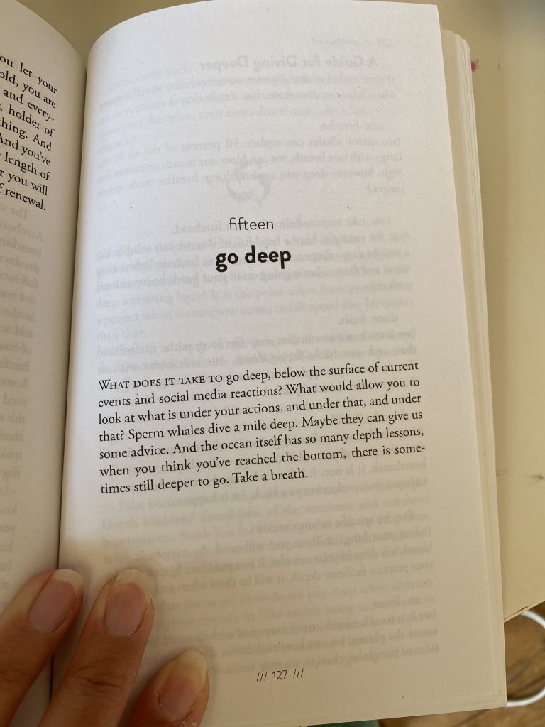 Hand of artist Rebekah Ubuntu holds open Alexis Pauline Gumbs’ book ‘Undrowned: Black Feminist Lessons from Marine Mammals’ on a page titled 'Go Deep'