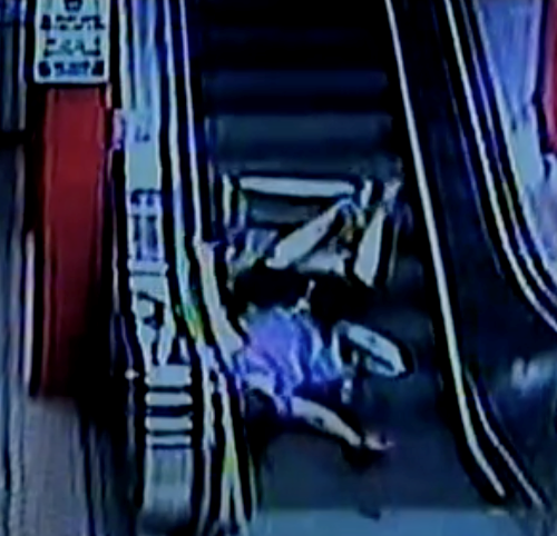 A muffled image in blue and black, a woman in a wheelchair falling backwards down an escalator