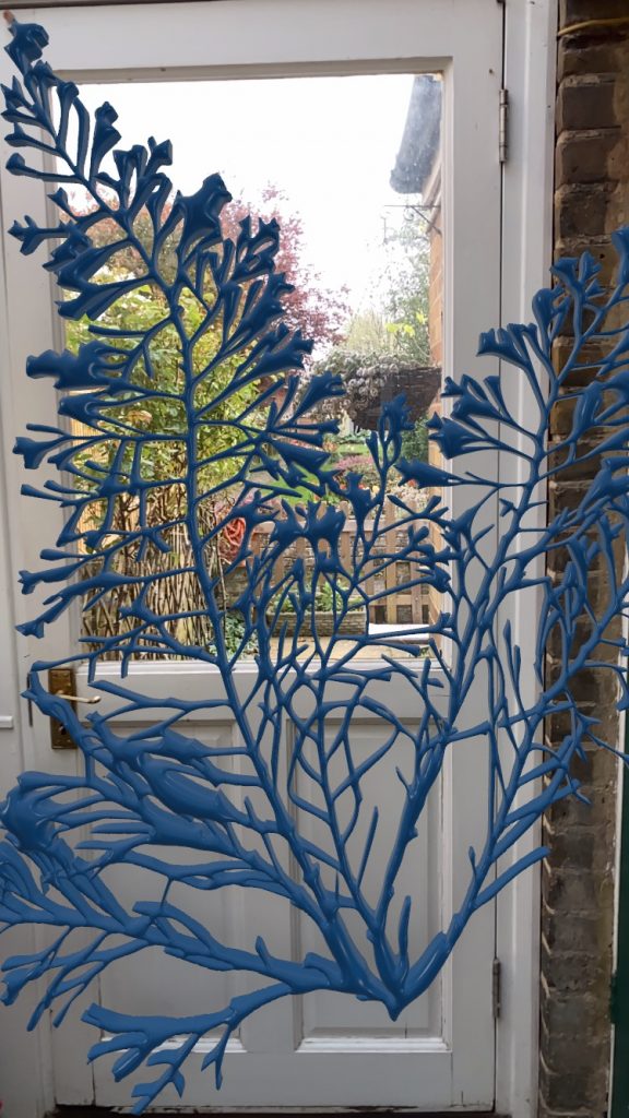 Photo of work in Vectary with its blue cyanotype material. The blue leaf is in front of a door with a window looking at a garden. 