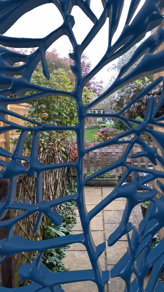 Close up photo of work in Vectary with its blue cyanotype material. The blue leaf is in front of a window looking at a garden. 
