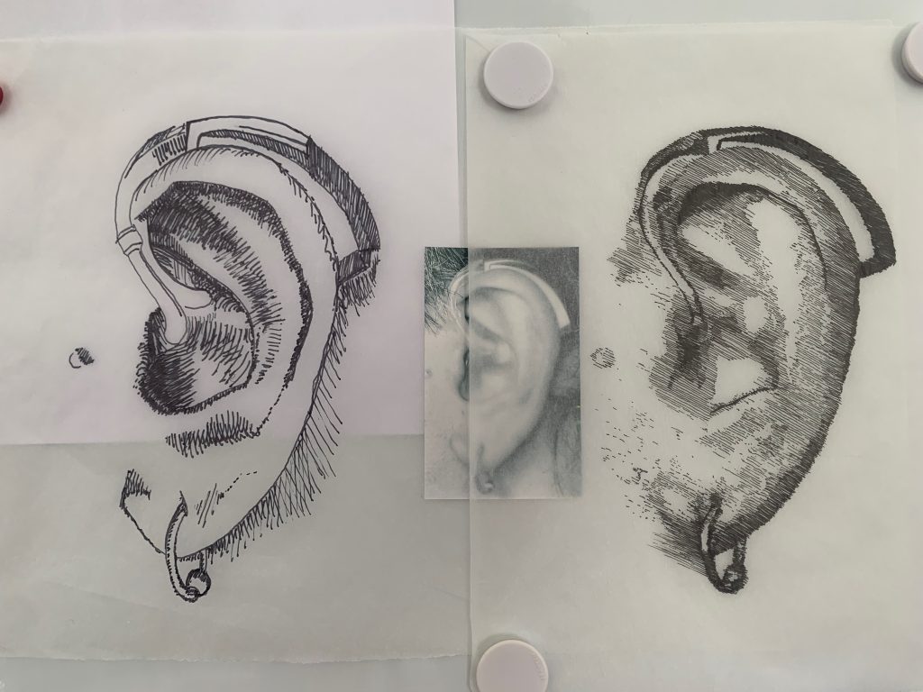 Two sketches and a photo of my left ear, layered on a whiteboard. A cyborg's ear is made of hearing aid and a piercing.