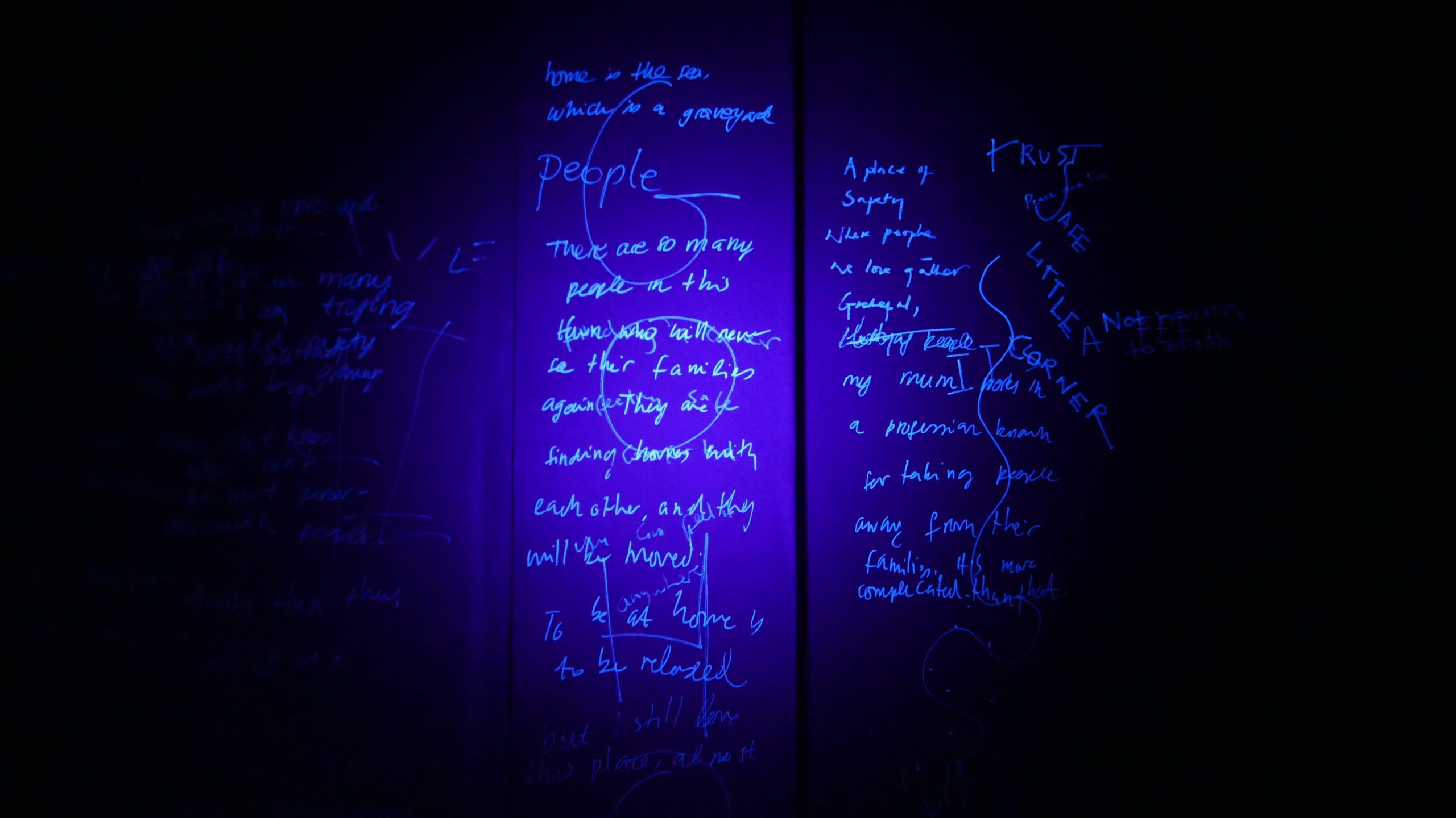 A black wall is covered in invisible ink that in lit up with a UV torch. 
The text is written with different handwriting, different sizes, directions and fonts.