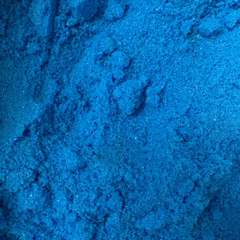 Close up of copper sulfate crystals, the size of sand but so turquoise that seems wet.