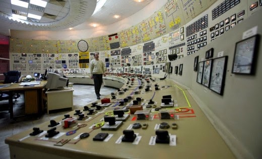 Inside a nuclear control system. A curved dashboard of endless buttons and switches. Mirroring this is a similarly curved wall of screens, displays and controls.