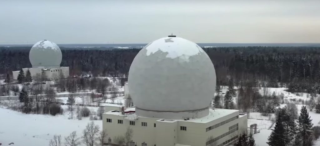 Two large geodesic domes housing satellite antennas sit within a snowy woodland landscape.