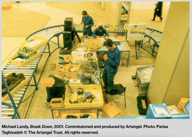 This image is a photograph of Michael Landy's installation work 'Break Down' from 2001. It shows a group of people categorising the artists items and putting them on a production line where they will eventually be destroyed. 
