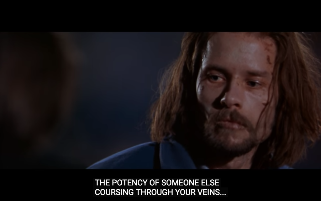 A close up of the face of a gaunt white man, with shoulder length brown hair and a beard, looking very unwell and pale, with cuts and blood on his face and very dry lips. The man looks off in the distance despondently. Below this are subtitles that read: "the potency of someone else coursing through your veins"