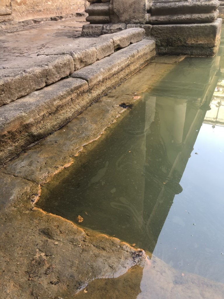 Up close at the corner of the bath. The cut stone corner descends in steps, the water consumes them in its milky green opacity.