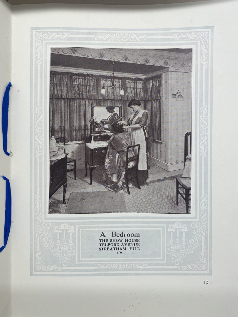 Vintage black-and-white photo of a bedroom with two women at a vanity—one seated in a gown, the other standing and assisting her. Large curtained windows fill the background. Caption reads: “A Bedroom – The Show House, Telford Avenue, Streatham Hill, S.W.”