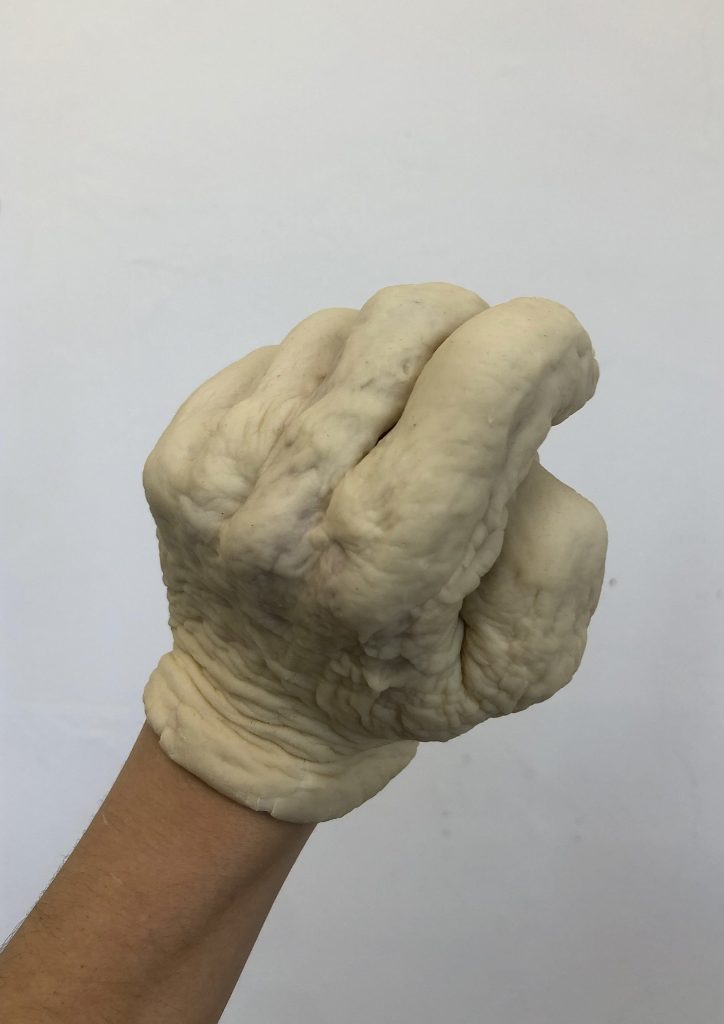 Two images of hands, covered in pizza dough. The first is splayed out, fingers spread, coming through the top right corner of the image. The second is the a hand coming from the bottom left of the image, a fist with knuckles facing us. Each look as though the hand of a gargoyle has been juxtaposed onto the wrist of a human. 