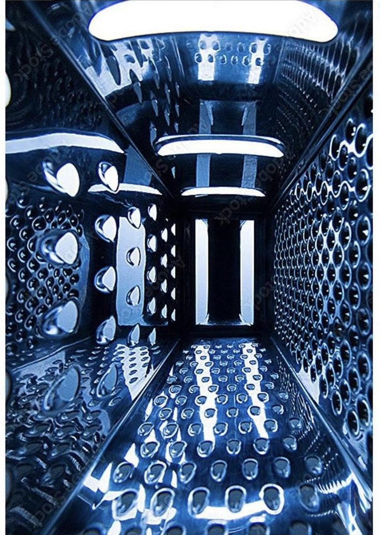 A close up photograph of the interior of a cheese grater, which also looks like a blue toned, futuristic corridor with reflective surfaces and geometric cut outs.