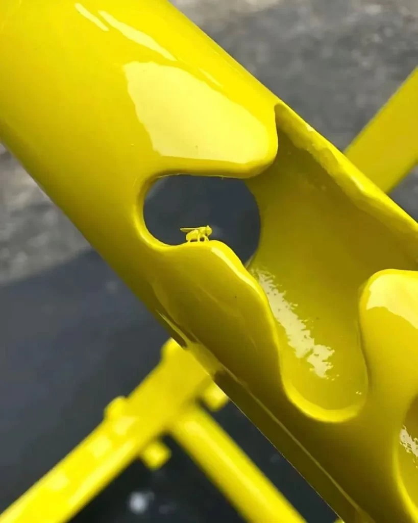 Close-up of a glossy bright yellow sculptural tube, most likely from some industrial structure, with a small fly resting on the edge, covered in the glossy yellow paint.